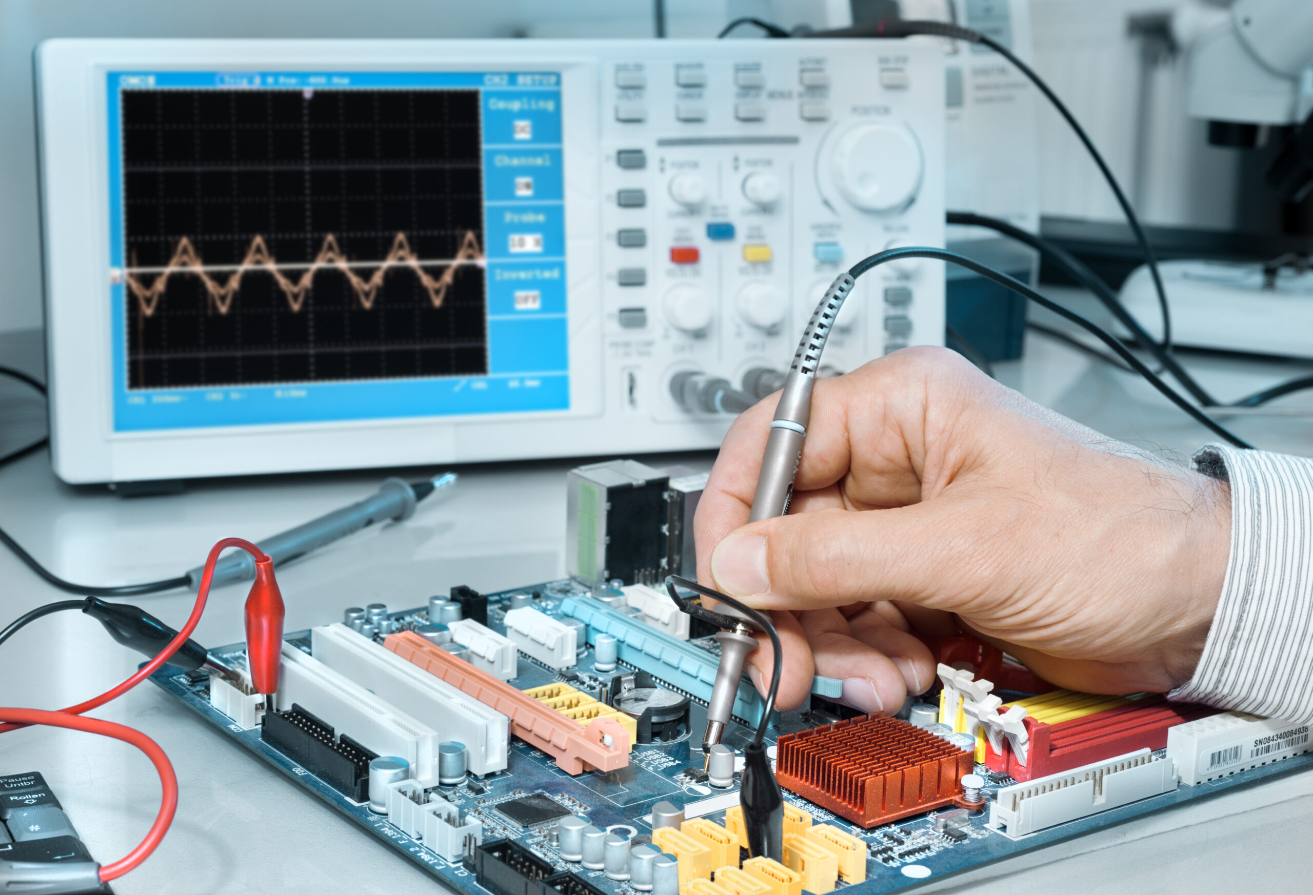 A technician tests a circuit board with a probe while an oscilloscope displays voltage waveforms, illustrating electronics diagnostics.