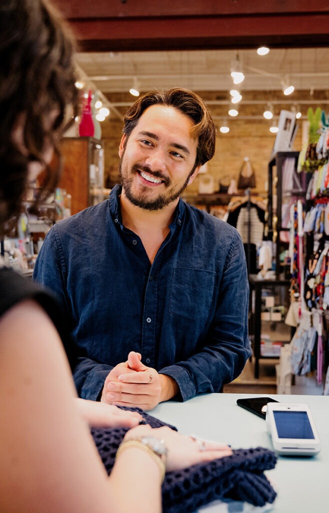 A smiling shopkeeper assists a customer at a counter, showcasing a friendly retail interaction in a vibrant store setting.