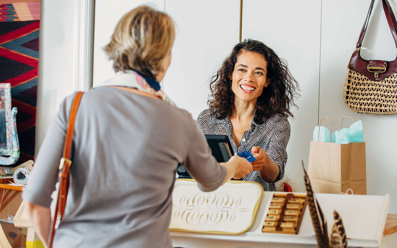 A smiling sales assistant hands a payment device to a customer at a retail checkout, showcasing a friendly shopping experience.