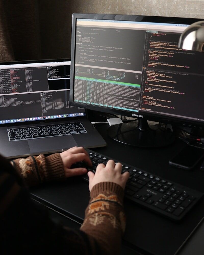 a person sitting at a desk with a laptop and a computer monitor